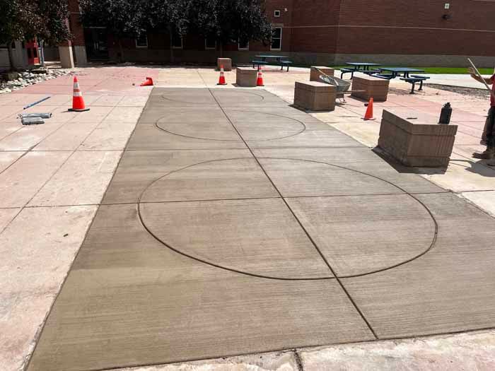 Newly poured concrete with two large circles and dividing lines, on a paved outdoor area.