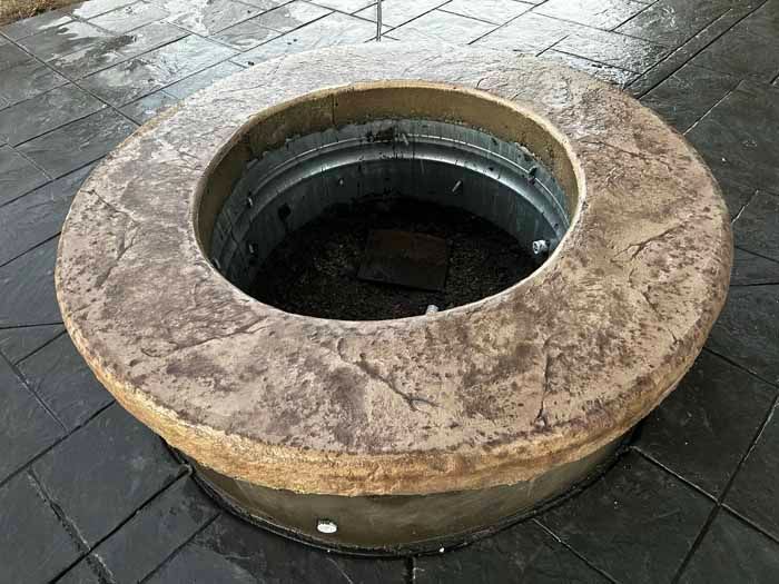 Round fire pit with a textured stone-like rim, set in a tiled patio.