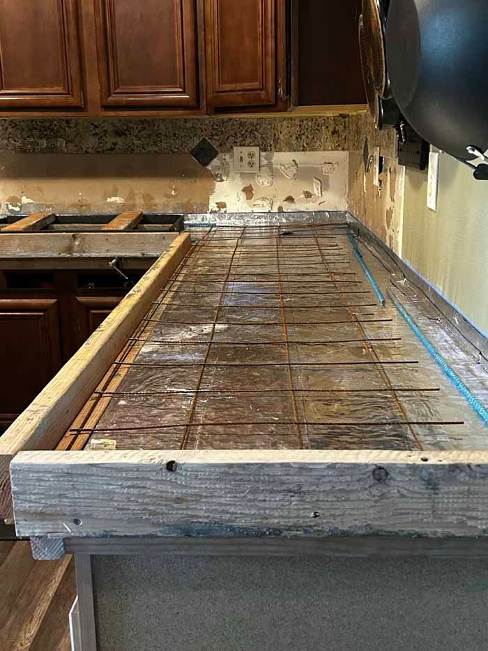 Kitchen countertop under construction; wooden form with rebar, brown cabinets in the background.