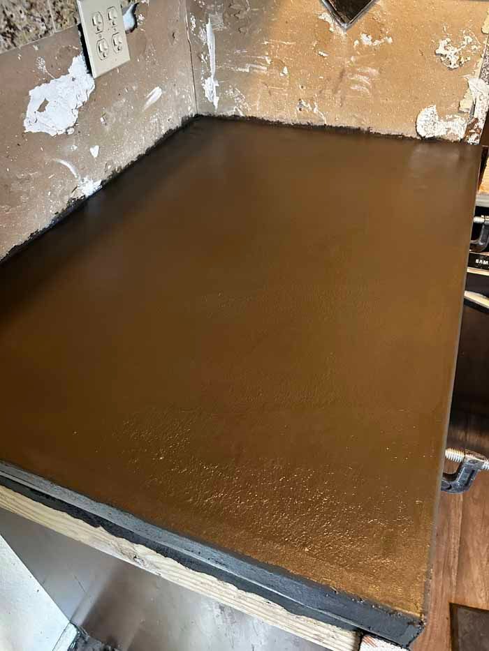Brown countertop, corner view, against peeling wall.