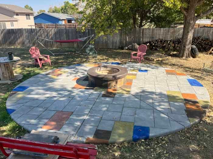 Circular patio with fire pit, colorful tile accents, surrounded by chairs and firewood.