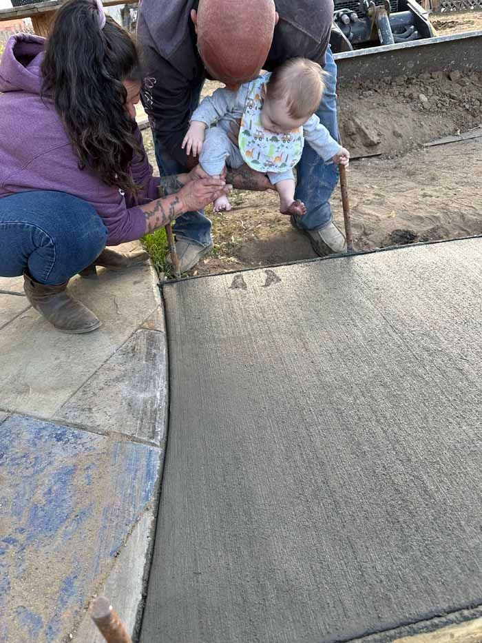 People holding a baby above wet concrete during sidewalk construction.