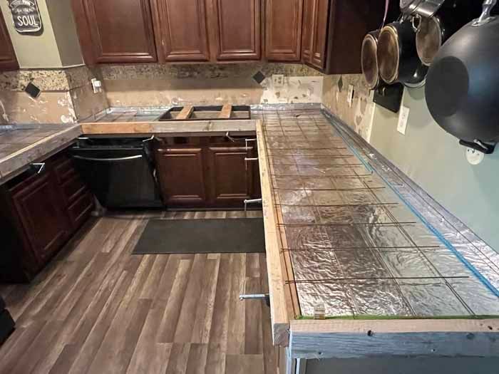 Kitchen remodel in progress: counter with metal grid and wood frame; cabinets, appliances, and walls visible.