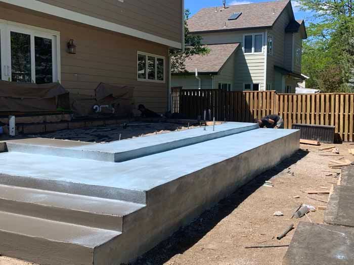 Construction of a concrete patio with steps, next to a house and a wooden fence.
