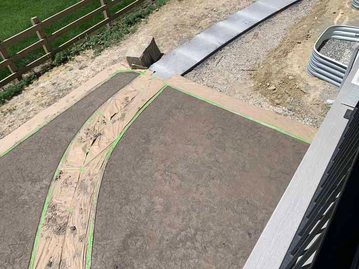 Stamped concrete patio with a curved path, metal drainage, and a section of a fence.
