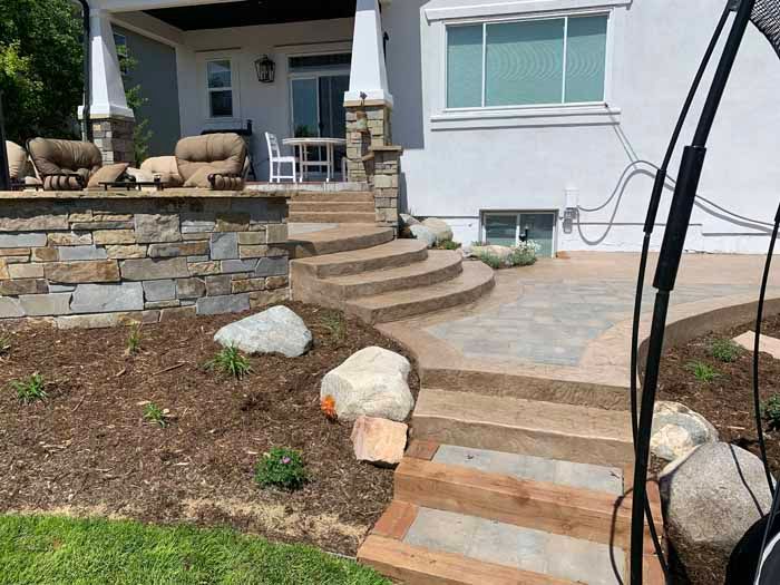 Stone steps and walkway leading to a house with a stone and wood patio, featuring large boulders and landscaping.