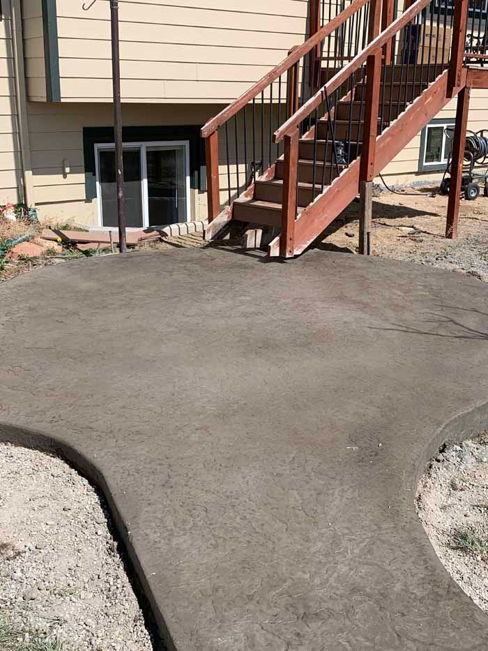 Newly poured concrete patio and walkway next to wooden deck stairs and a house with a sliding glass door.