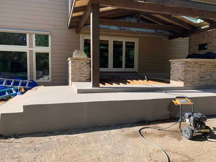 Exterior concrete patio with steps leading to a covered area, and a pressure washer.