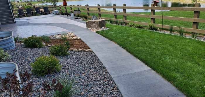 A paved pathway curves through a landscaped yard with grass and a wooden fence.