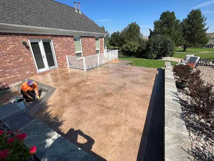 Man working on a newly stained concrete patio next to a brick house on a sunny day.