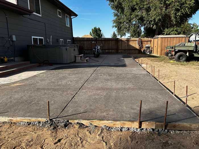 Newly poured concrete patio in a backyard setting, next to a hot tub.
