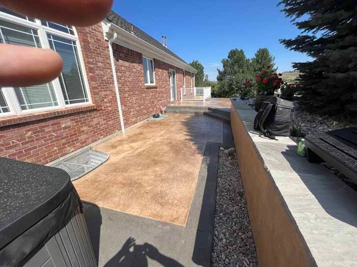 Backyard patio with brick house, concrete, and low retaining wall under blue sky.