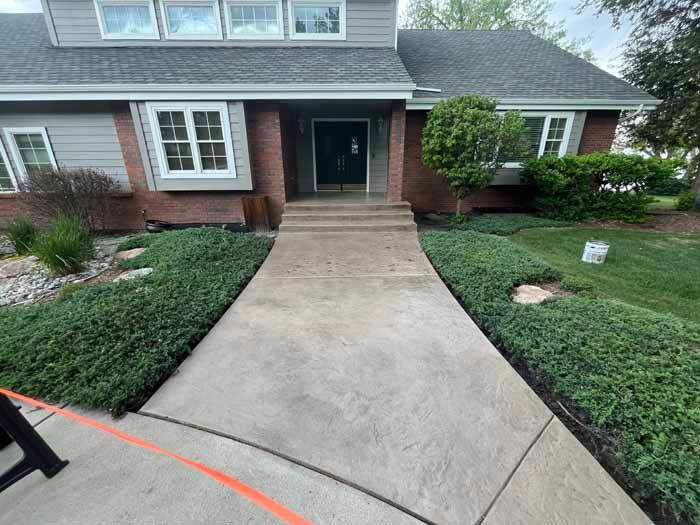 A concrete walkway leads to a brick home's front door; shrubbery borders the path.