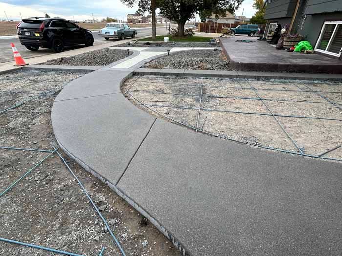 Newly poured concrete walkway curving towards a house, surrounded by gravel and rebar.