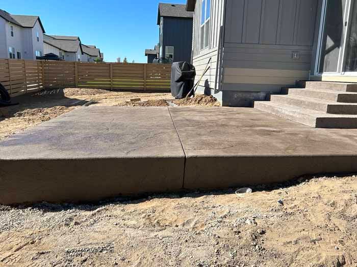 Concrete patio with steps, next to a house with a wooden fence in the background.