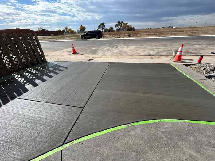 Freshly poured concrete sidewalk with green tape border and traffic cones.