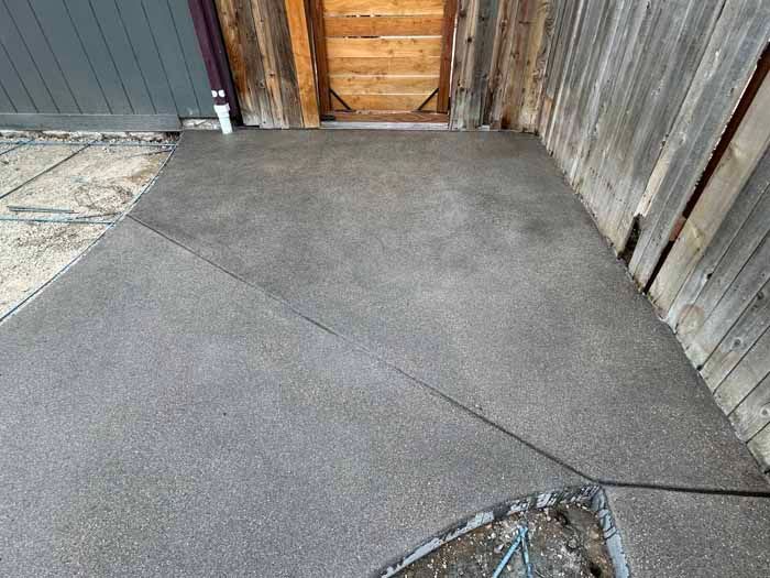 Concrete patio with diagonal lines, next to a wooden building and a doorway.