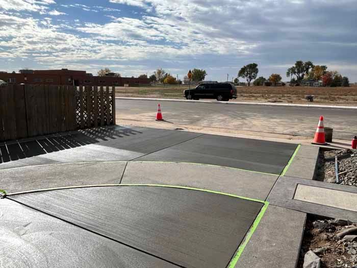 Newly poured concrete pathway, sections separated by green tape, with a vehicle in the background.