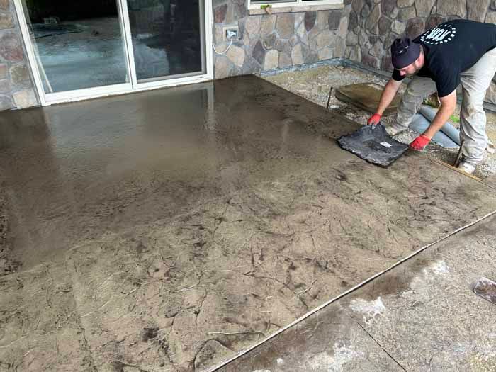 Man applying a textured pattern to a wet concrete patio using a stamp tool.