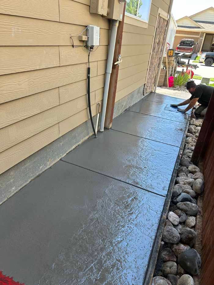 Freshly poured gray concrete walkway next to a building. A person is brushing the concrete.