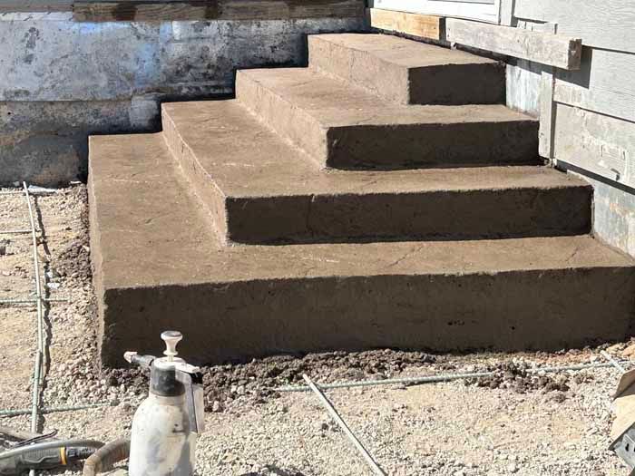 Concrete steps, newly poured, leading up to a building entrance. Rebar is visible around the base.