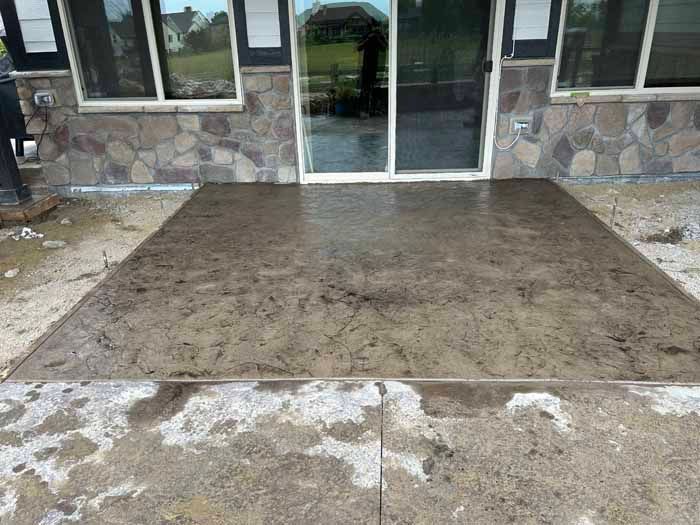Concrete patio with sliding glass door and stone facade. Wet surface, medium shot.