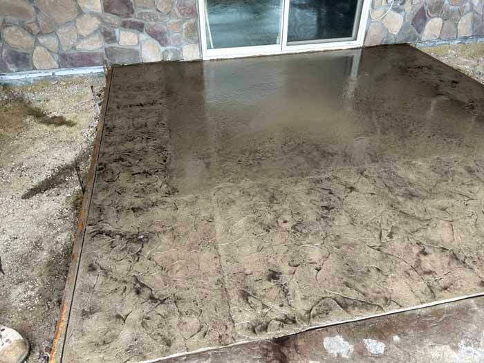Polished concrete patio with brown and tan tones next to a building with stone siding and a sliding glass door.