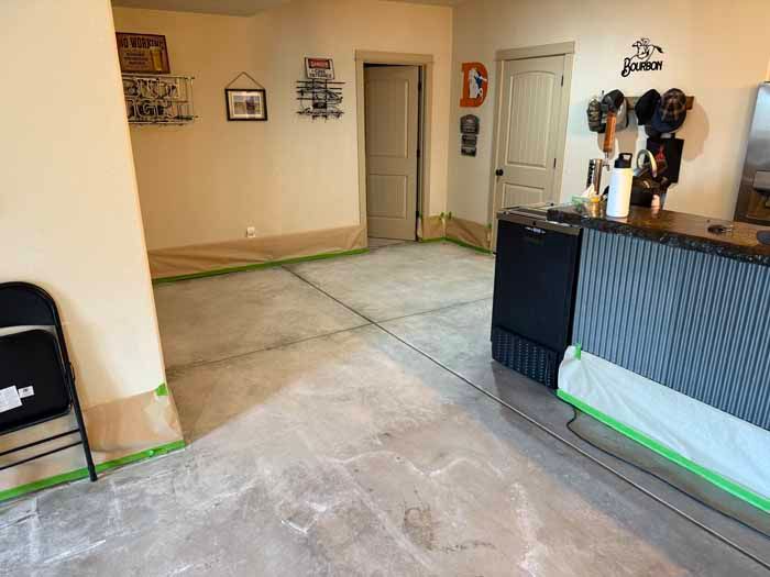 Interior view of a room with exposed concrete floor, walls protected with tape, bar, doorway.