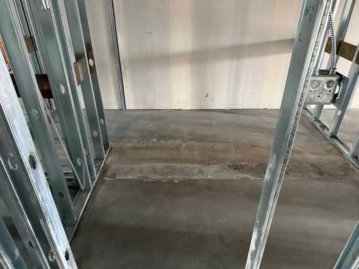 Interior view of a construction site with metal framing and concrete floor. The floor has visible cracks.