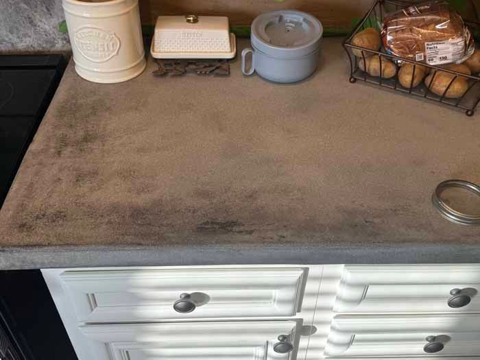 Concrete kitchen countertop with cream-colored cabinetry, featuring kitchenware and produce.