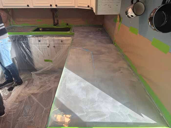 Kitchen countertop resurfacing with gray coating, covered appliances and walls.