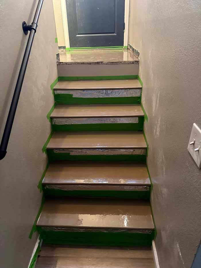 Staircase with wooden steps protected by green painter's tape; a black handrail on the left.