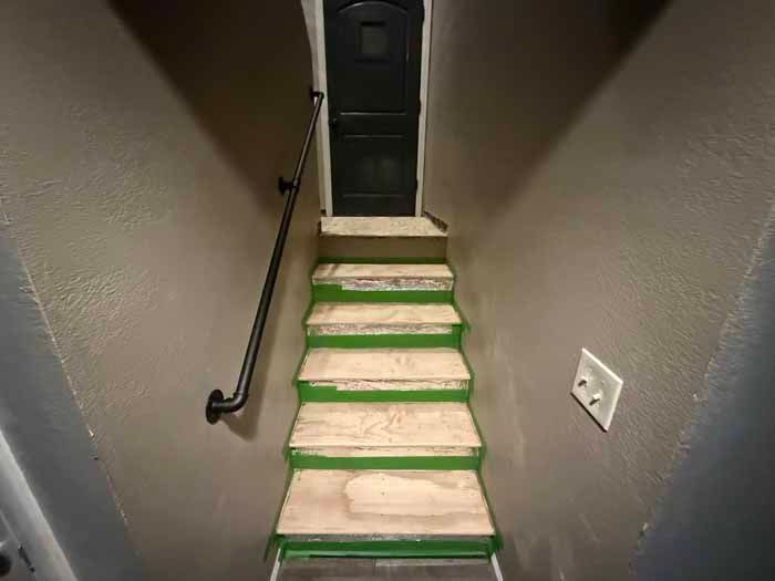 Narrow staircase with green-trimmed, wooden steps, handrail, and a dark door at the top.