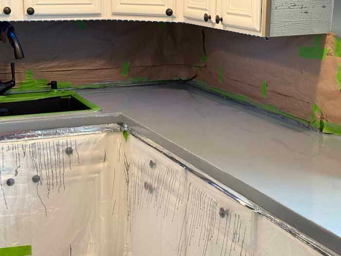 Kitchen countertop resurfacing with gray coating, cabinets covered with paper and plastic for protection.