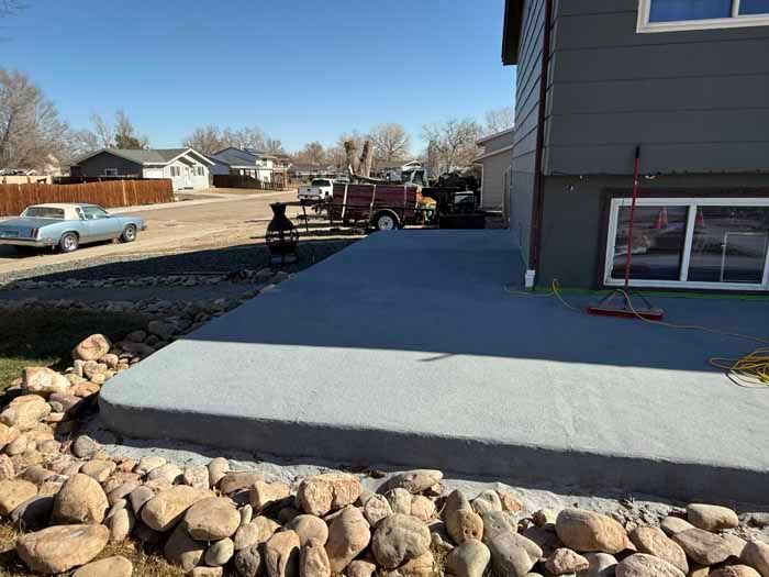A gray concrete patio next to a dark gray house, with landscaping rocks in front.