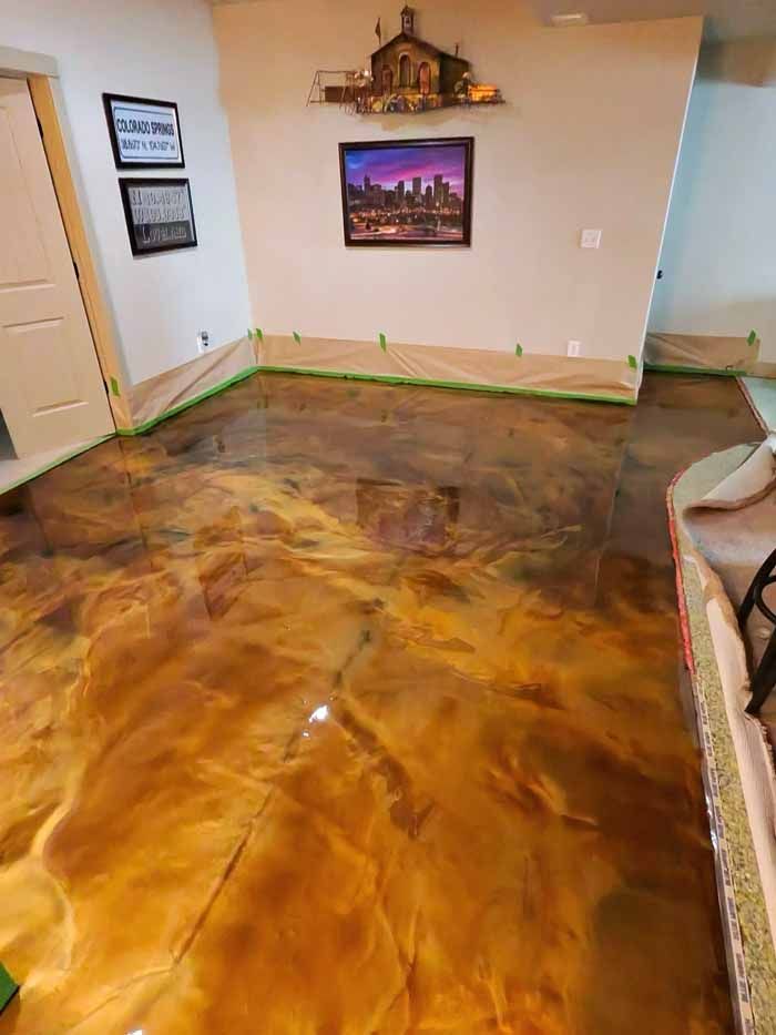 Metallic gold epoxy floor, with brown and amber tones. Room has beige walls, artwork, and door.