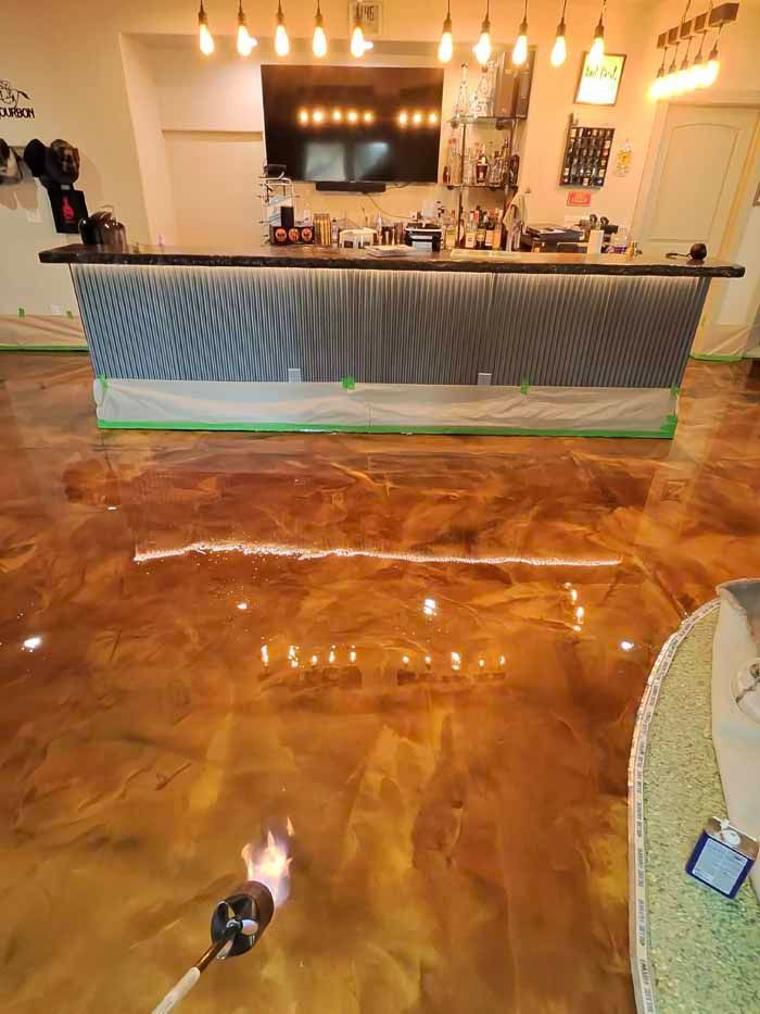 Epoxy flooring in a bar setting, gold and brown tones, with a torch being used during installation.