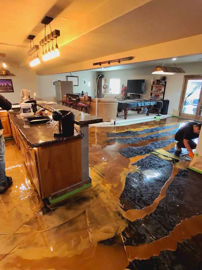 Kitchen with epoxy flooring installation, gold and black colors. Person kneeling, applying epoxy.