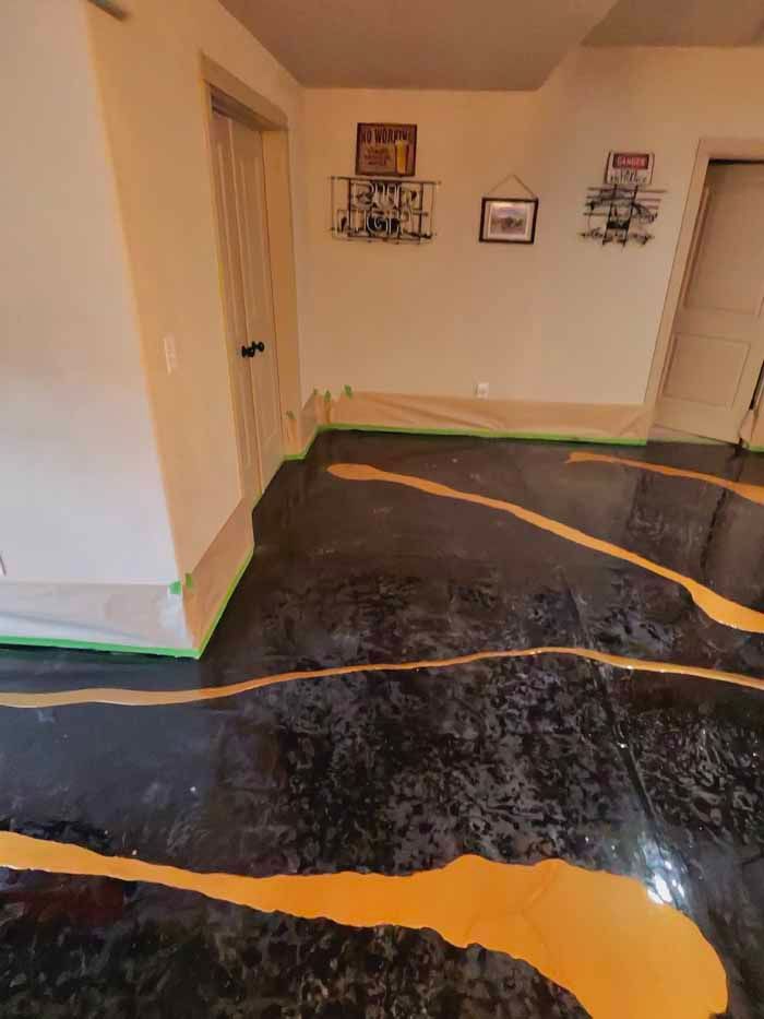 Epoxy floor in progress: Black base with gold accent lines. Green tape protects walls.