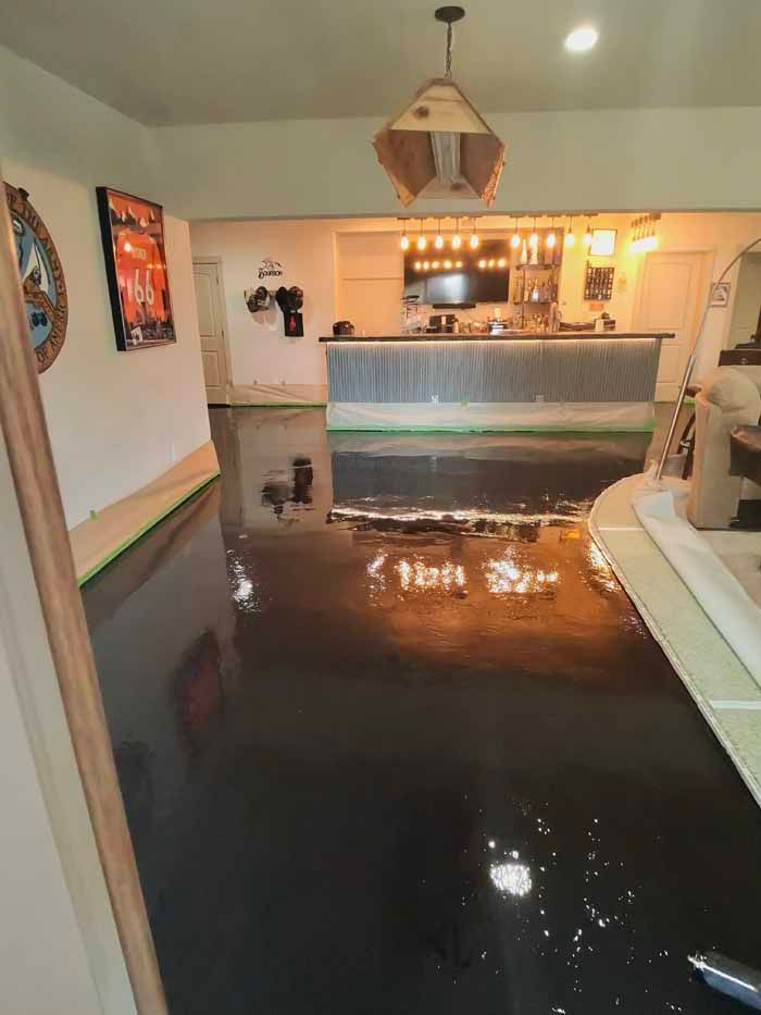 Dark epoxy floor reflects light from a bar and fixture; a partially finished home interior.