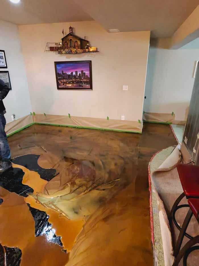 Epoxy floor installation in a room with art on the wall and furniture covered for protection.