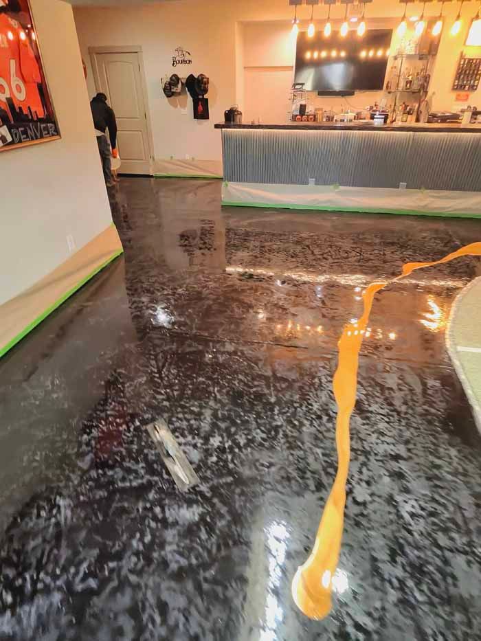 Shiny, black epoxy floor with gold streak. Interior shot with bar, door, and person in the distance.