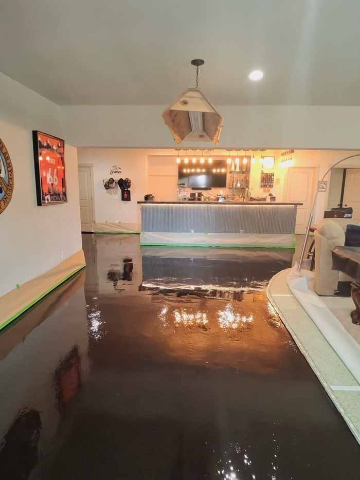 Shiny, metallic epoxy floor reflects kitchen and light fixtures. Room features a bar and art.