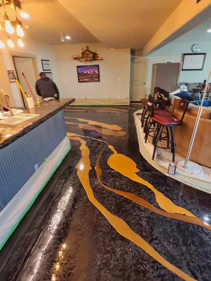 Basement with epoxy floor in black and gold design, bar, stools, and person.