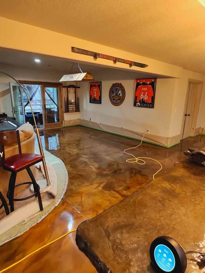 Basement with brown epoxy floor, bar, barstool, doorway, sports jerseys on wall, yellow cord.