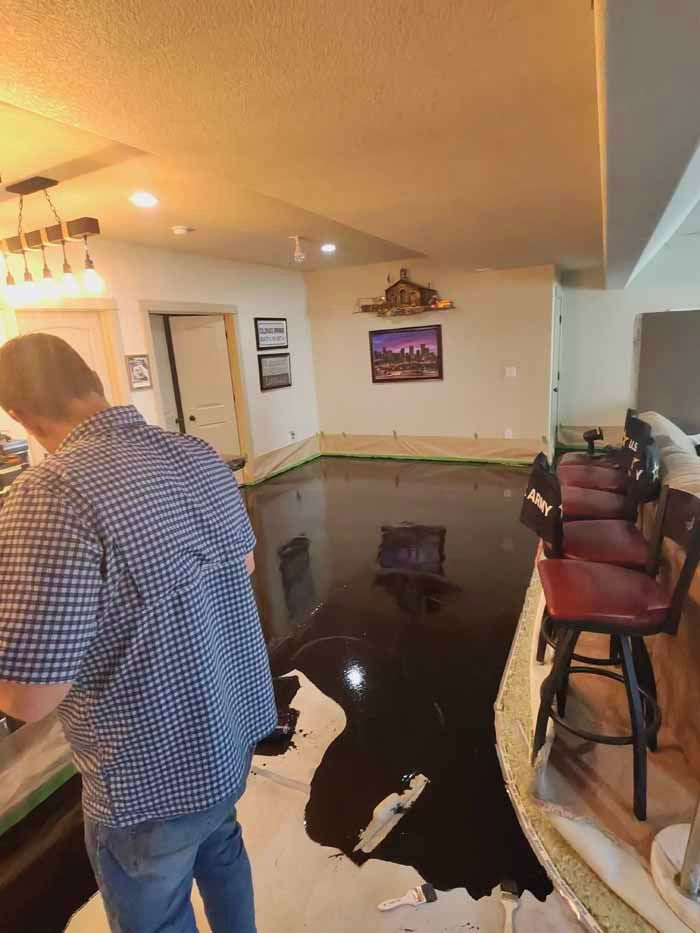 Person in blue shirt stands near a shiny, dark floor. Bar stools line a counter. Walls are white, with artwork.