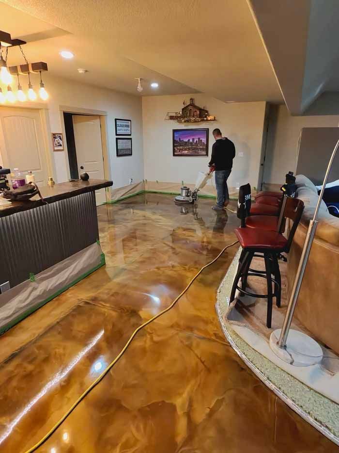 Person polishing a gold epoxy floor in a room. Bar, art, and furniture visible.