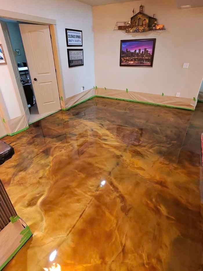 Metallic epoxy floor in shades of gold and brown, with wall protection tape along the edges.