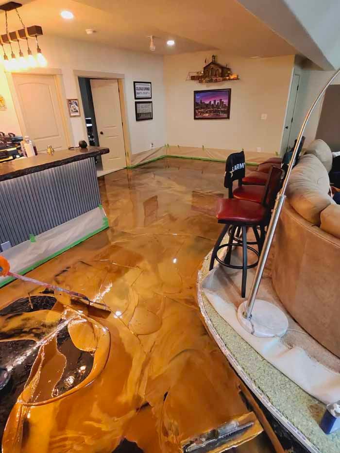 Shiny, gold epoxy flooring in a basement.  Bar with red stools. Green tape lines walls.