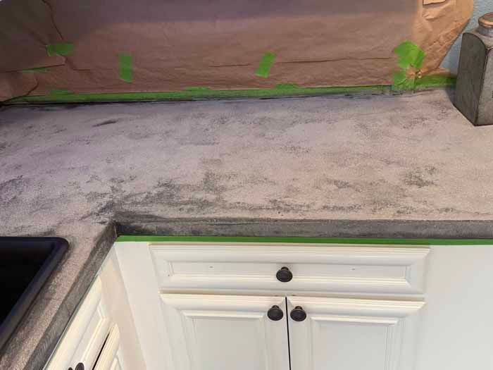 Countertop being resurfaced with gray and black paint, taped to protect cabinets.